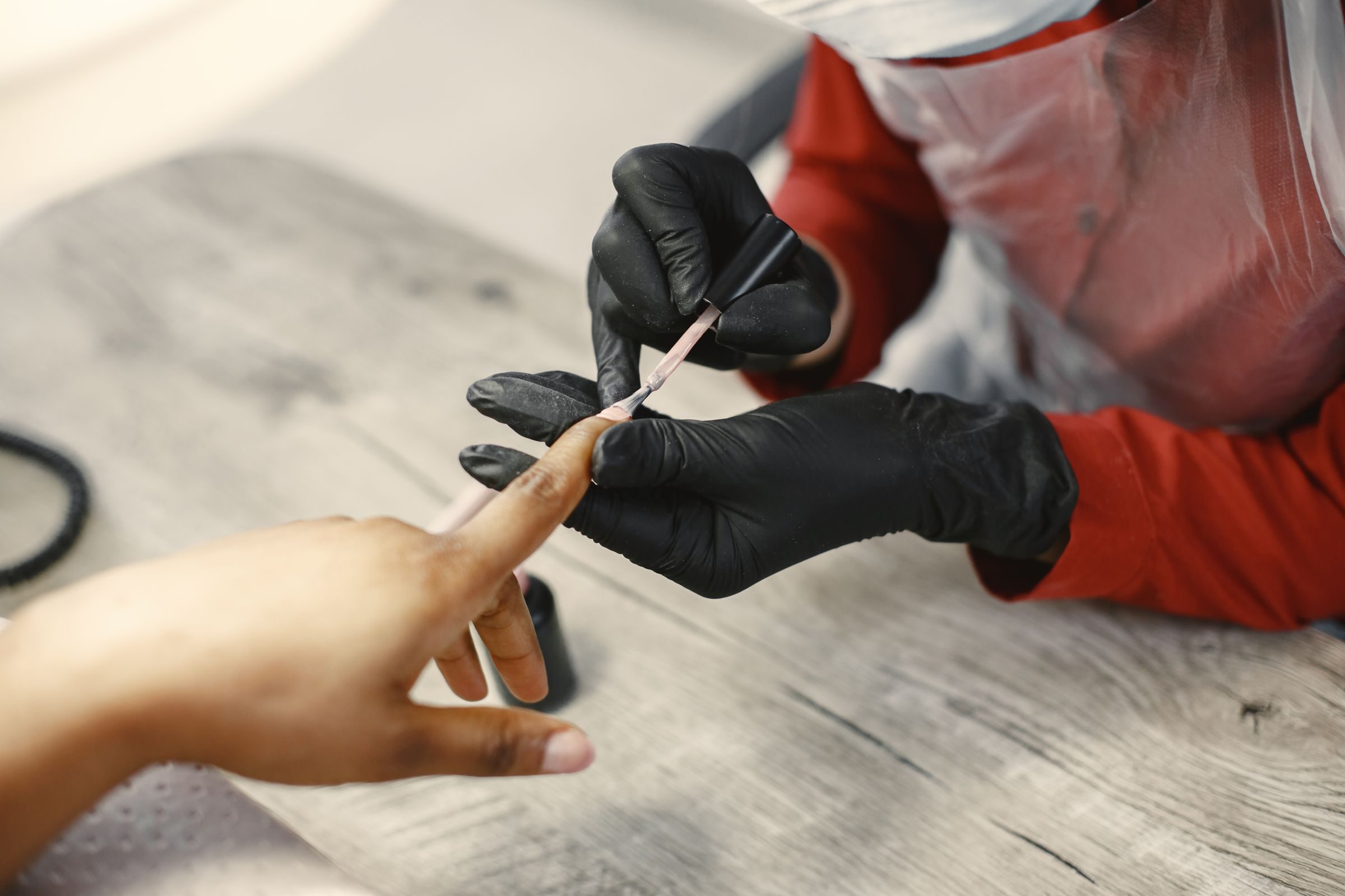 Prothésiste ongulaire gantée qui travaille un ongle au pinceau